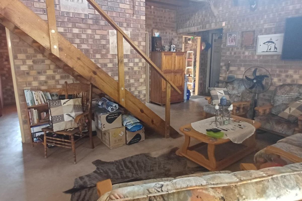 A rustic living room featuring exposed brick walls, concrete flooring, and a wooden staircase with a matching balustrade.
