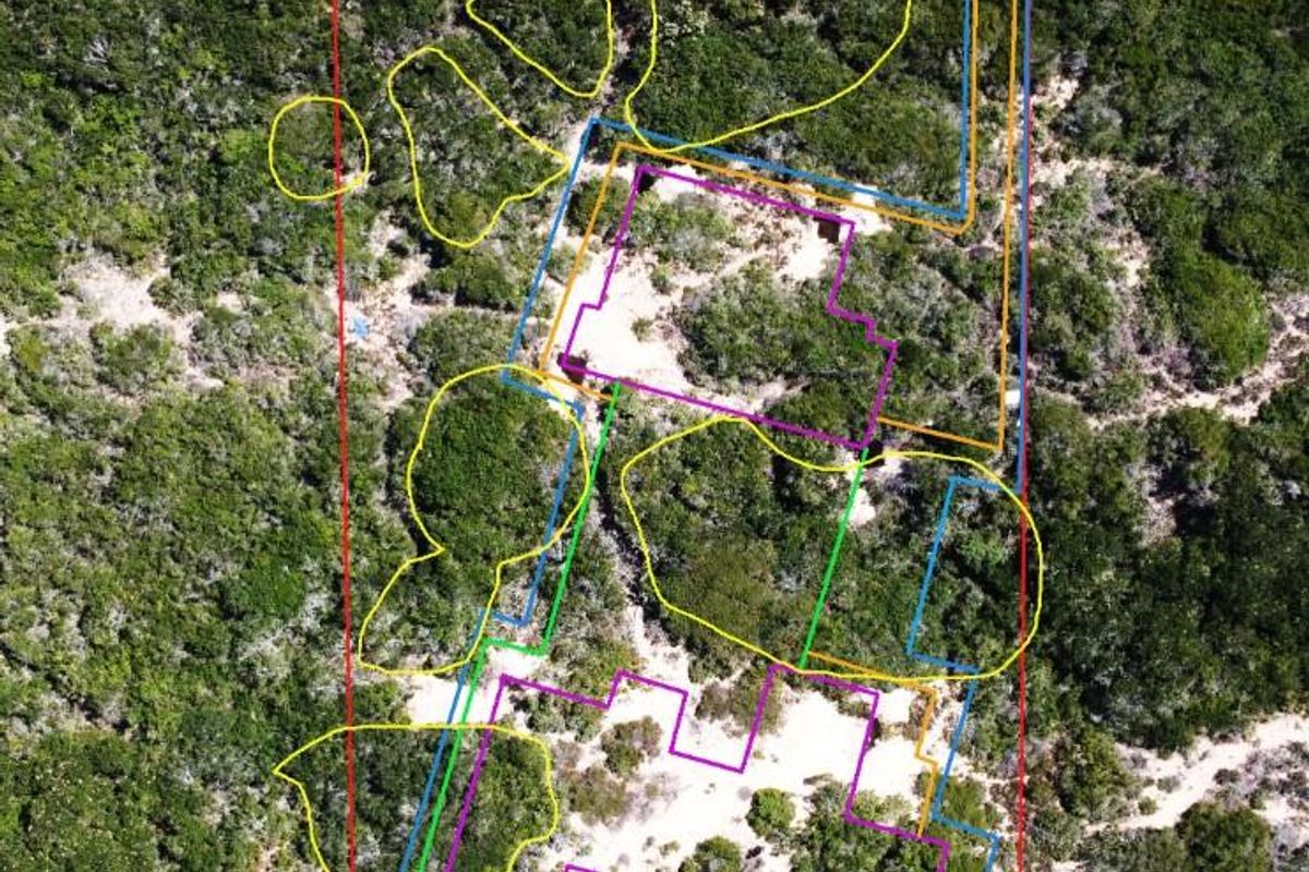 Aerial view of a vacant residential plot featuring natural vegetation and sand, with overlaid boundary markings indicating the property layout.