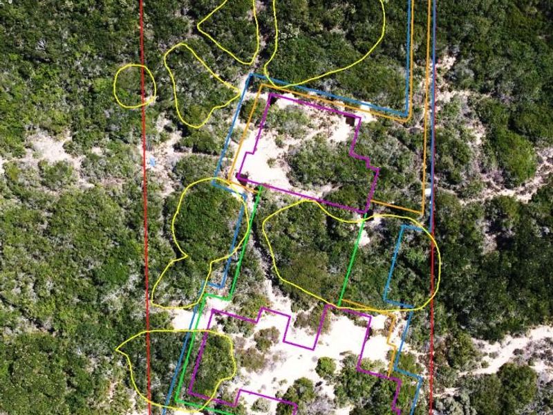 Aerial view of a vacant residential plot featuring natural vegetation and sand, with overlaid boundary markings indicating the property layout.
