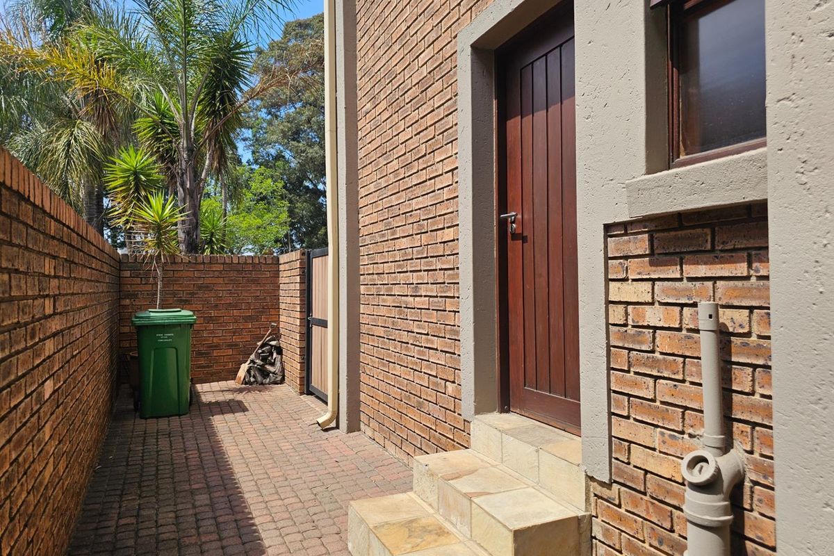 A side exterior view of the property featuring a brick facade, paved walkway, and a wooden door with stone steps.
