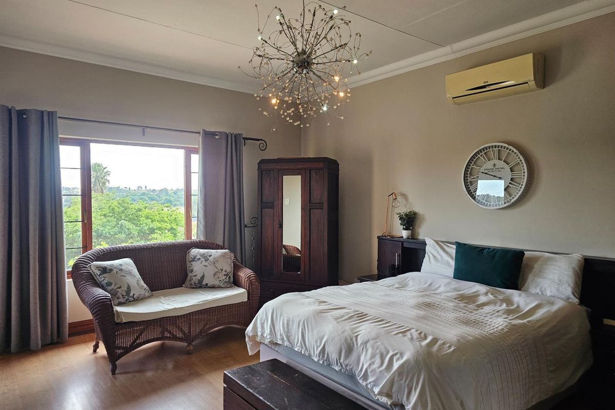 A spacious bedroom featuring laminate flooring, a large window with garden views, and a wall-mounted air conditioning unit.