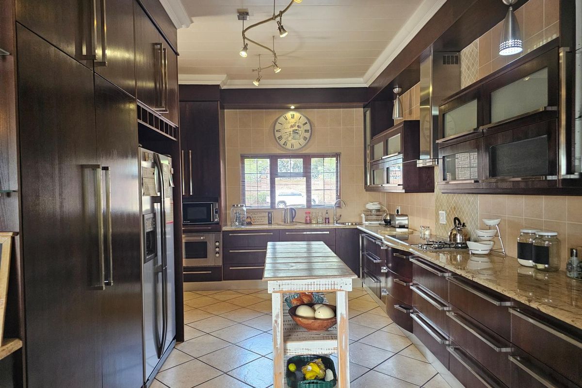 A spacious kitchen featuring dark wood cabinetry, granite countertops, a central island, and tiled flooring with integrated stainless steel appliances.