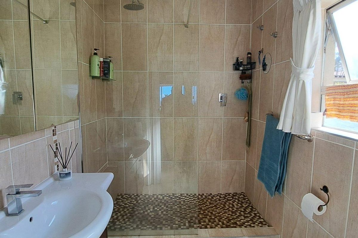 A functional bathroom featuring a walk-in shower with a glass screen, wall-mounted shower head, and a pedestal basin with a modern mixer tap.