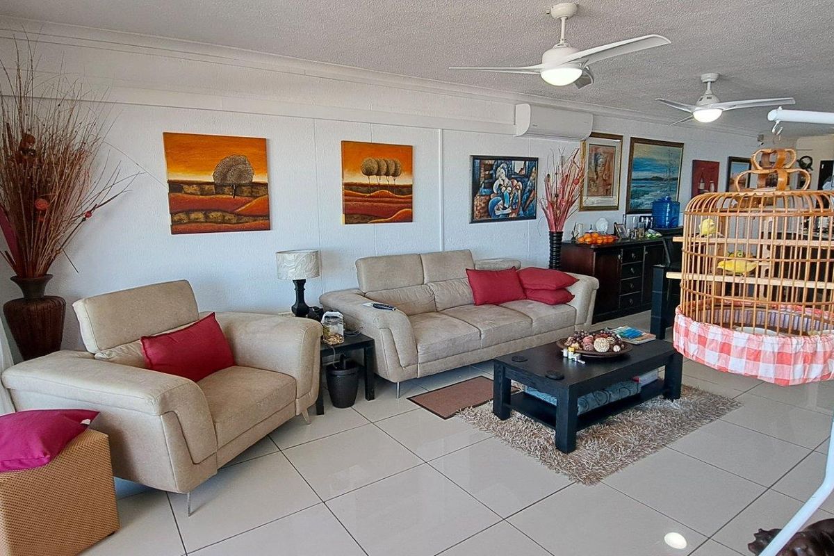 Spacious living area featuring large format floor tiles, dual ceiling fans, and a wall-mounted air conditioning unit with access to an outdoor balcony.