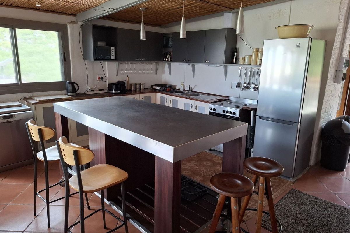 A functional kitchen featuring a central island with a metal countertop, dark cabinetry, and a bamboo-style ceiling finish.