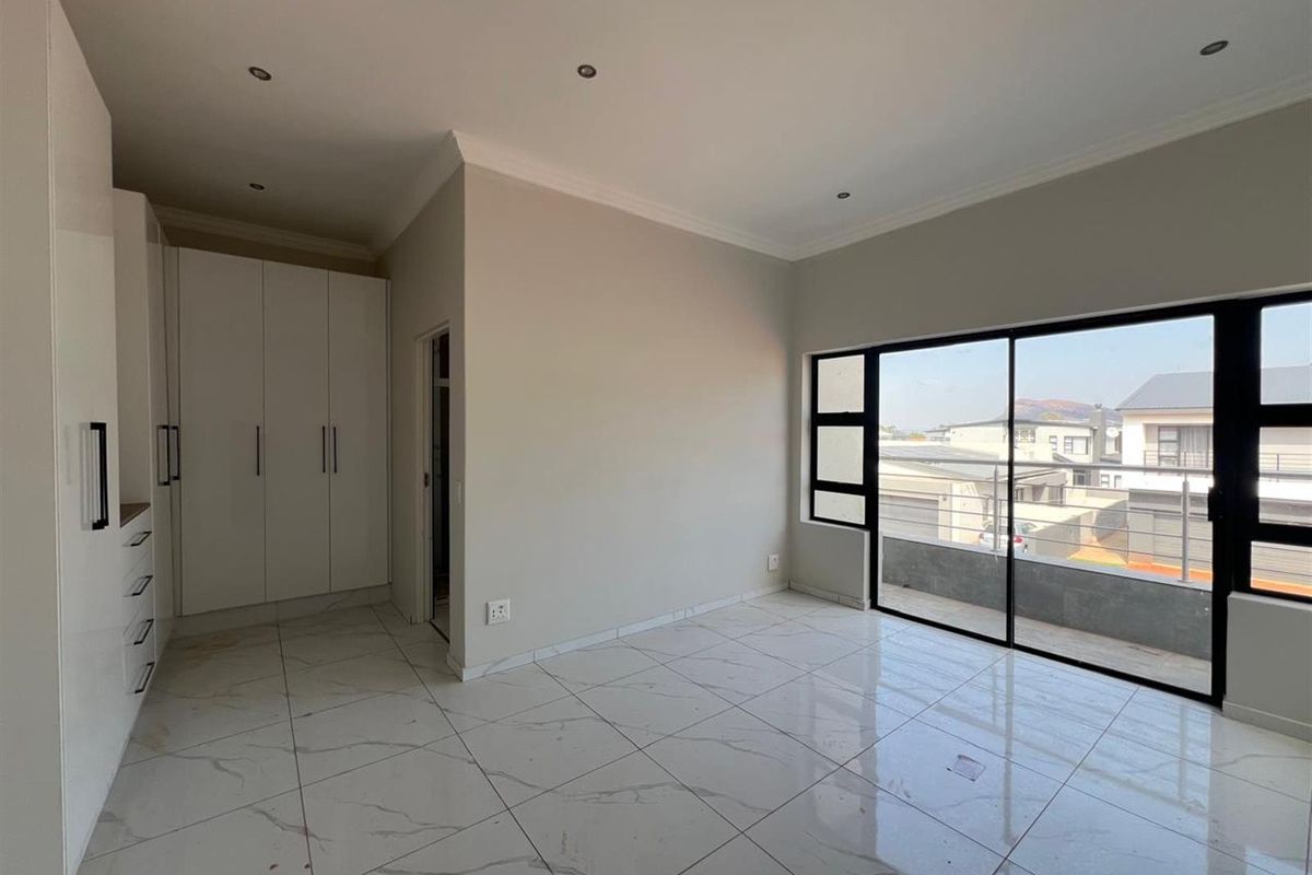 A bright, modern bedroom featuring large format marble-look floor tiles, built-in white cabinetry, and sliding glass doors opening to a balcony.