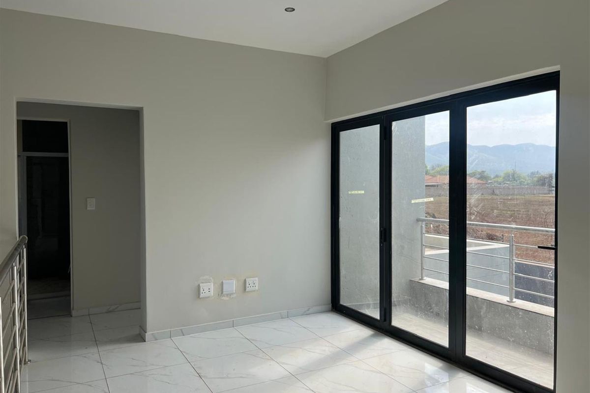 A bright, modern living area featuring large black-framed sliding glass doors that open onto a balcony, complemented by sleek white tiled flooring.