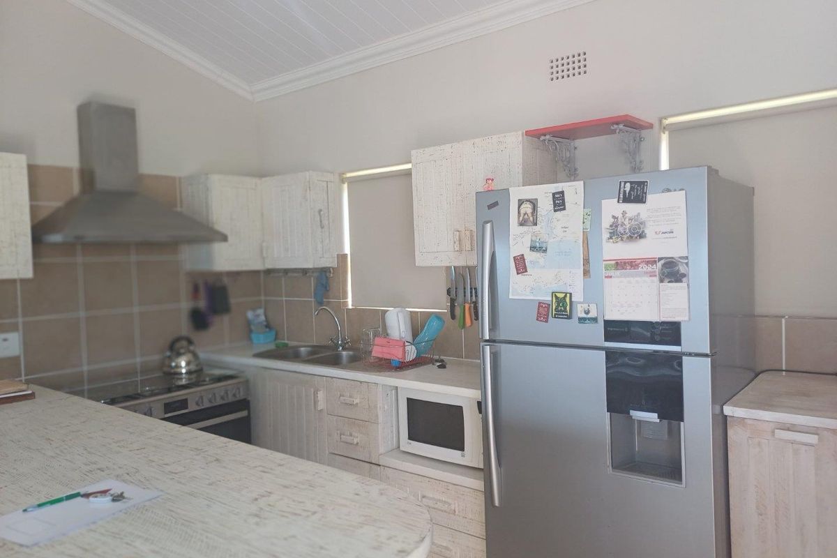 A functional kitchen featuring white distressed-style cabinetry, a stainless steel extractor fan, built-in oven, and a breakfast bar counter.