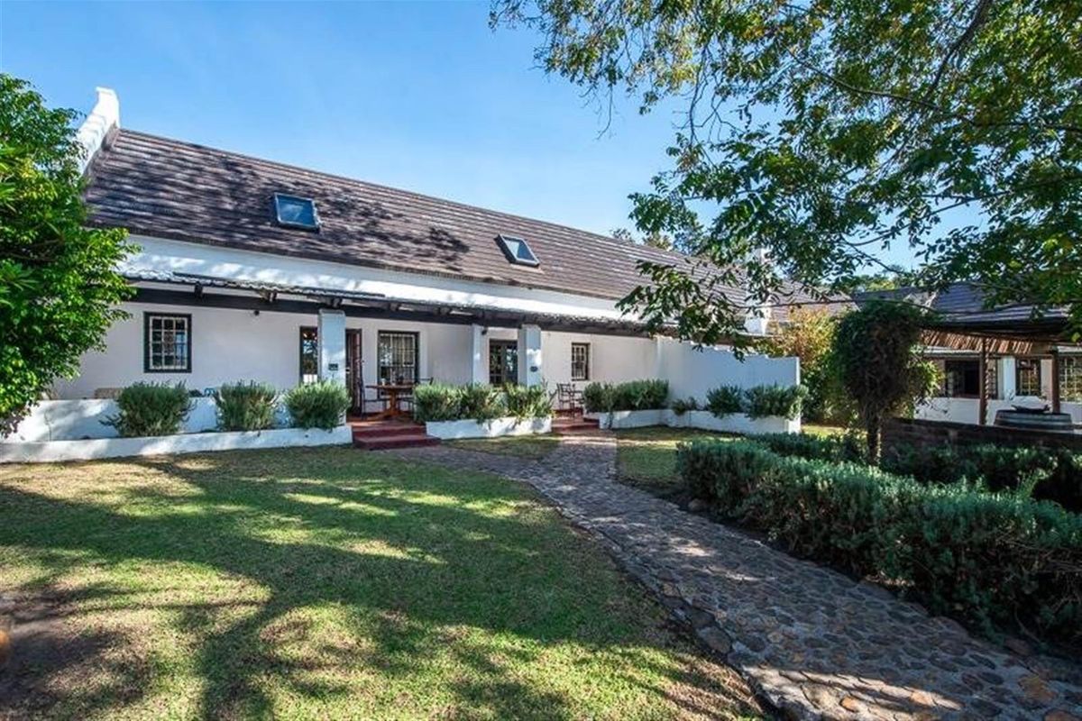 A charming rear exterior view of the small holding featuring a pitched tiled roof with skylights, a covered patio, and a stone paved garden walkway.