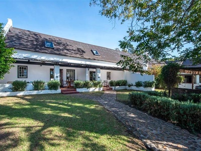 A charming rear exterior view of the small holding featuring a pitched tiled roof with skylights, a covered patio, and a stone paved garden walkway.