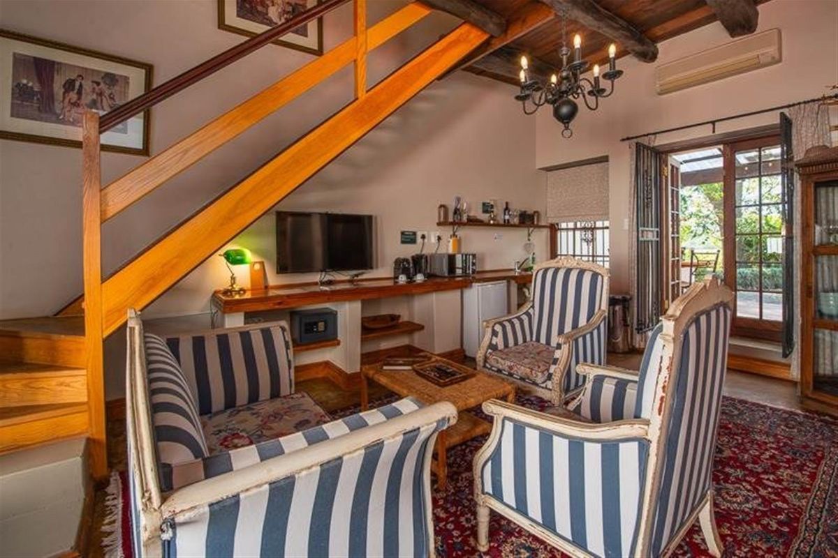 Cozy living area featuring exposed timber ceiling beams, a wooden staircase, built-in desk space, and direct access to the outdoor patio through french doors.