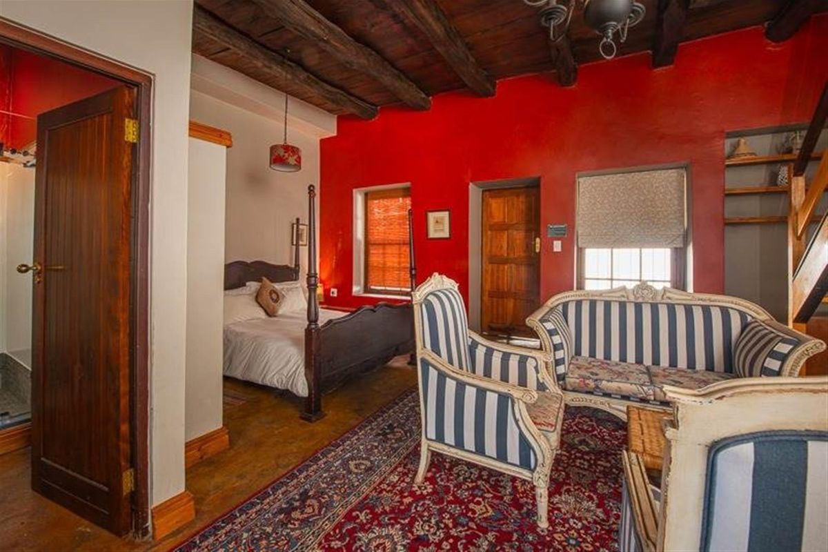 A rustic bedroom featuring exposed timber ceiling beams, vibrant red accent walls, and an adjoining bathroom entrance.