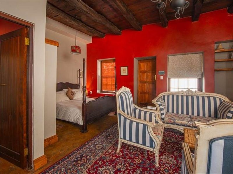 A rustic bedroom featuring exposed timber ceiling beams, vibrant red accent walls, and an adjoining bathroom entrance.