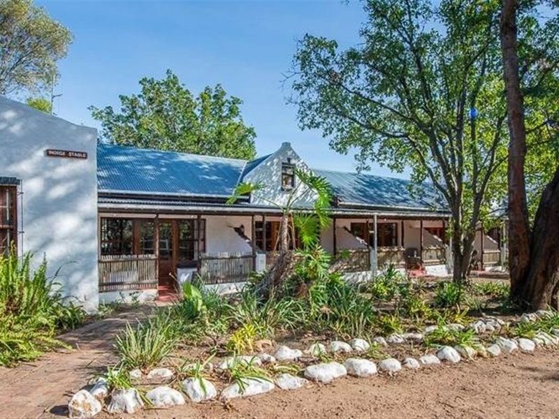 Charming single-story small holding residence featuring a classic gabled facade, corrugated iron roof, and a welcoming covered veranda set within a mature garden.