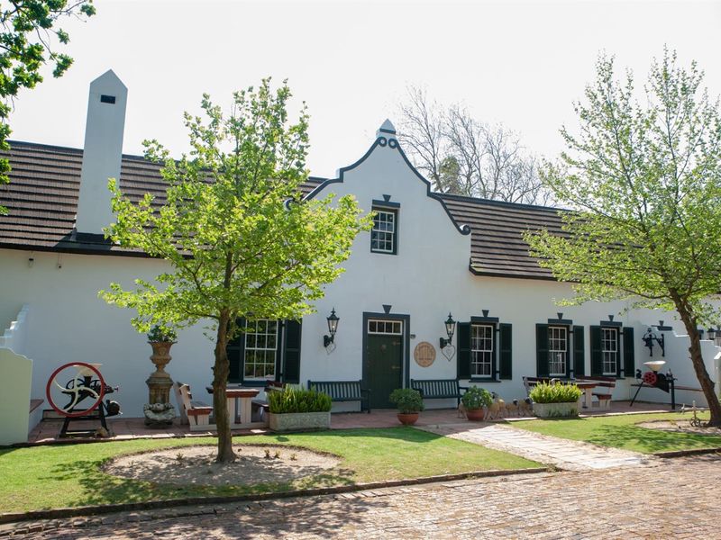 A charming Cape Dutch style small holding residence featuring a classic gabled facade, tiled roof, and a paved front patio area.