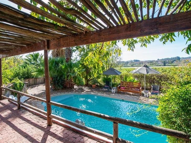 Outdoor pool area featuring a rustic wooden pergola, brick-paved patio, and established garden surroundings with scenic landscape views.
