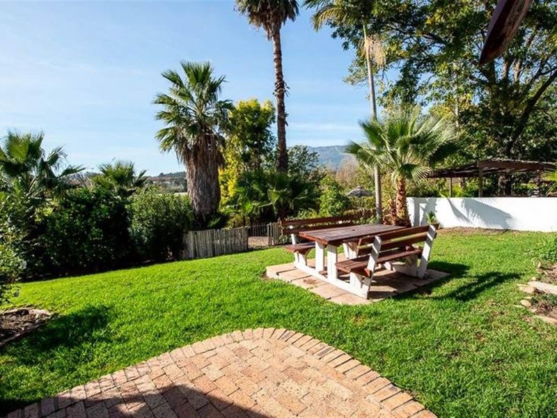 A well-maintained garden area featuring a brick-paved section, lush lawn, and mature palm trees with mountain views in the background.