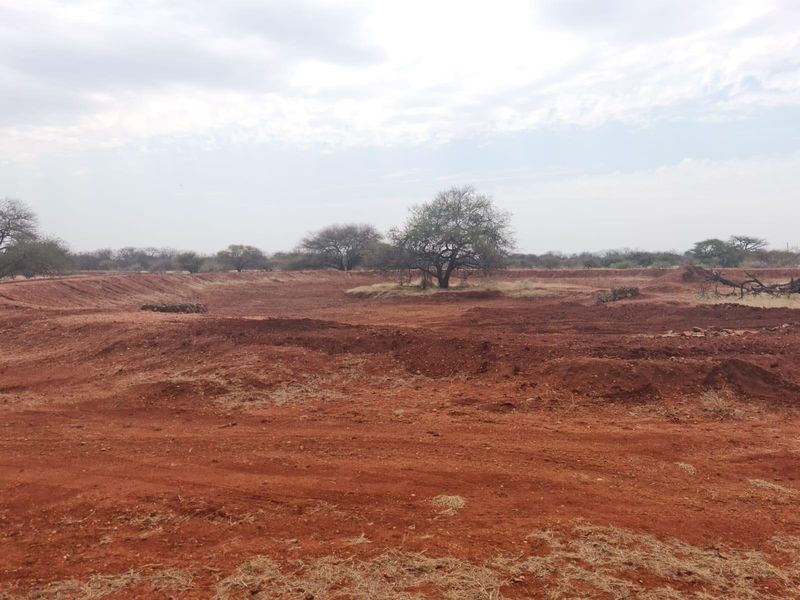 An expansive, undeveloped plot of rural farm land featuring natural red soil, sparse vegetation, and open terrain suitable for agricultural or development purposes.