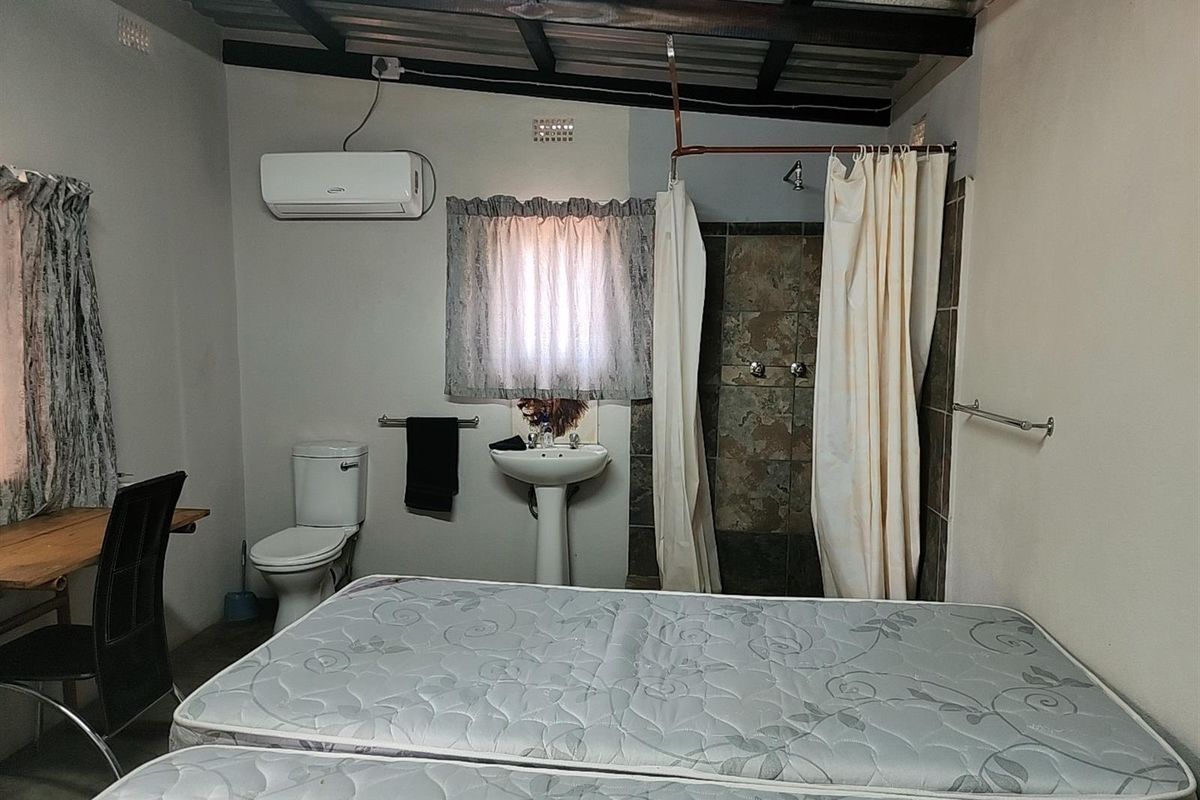 A functional bedroom featuring an integrated open-plan bathroom with a shower, pedestal basin, and toilet, complemented by an air conditioning unit.