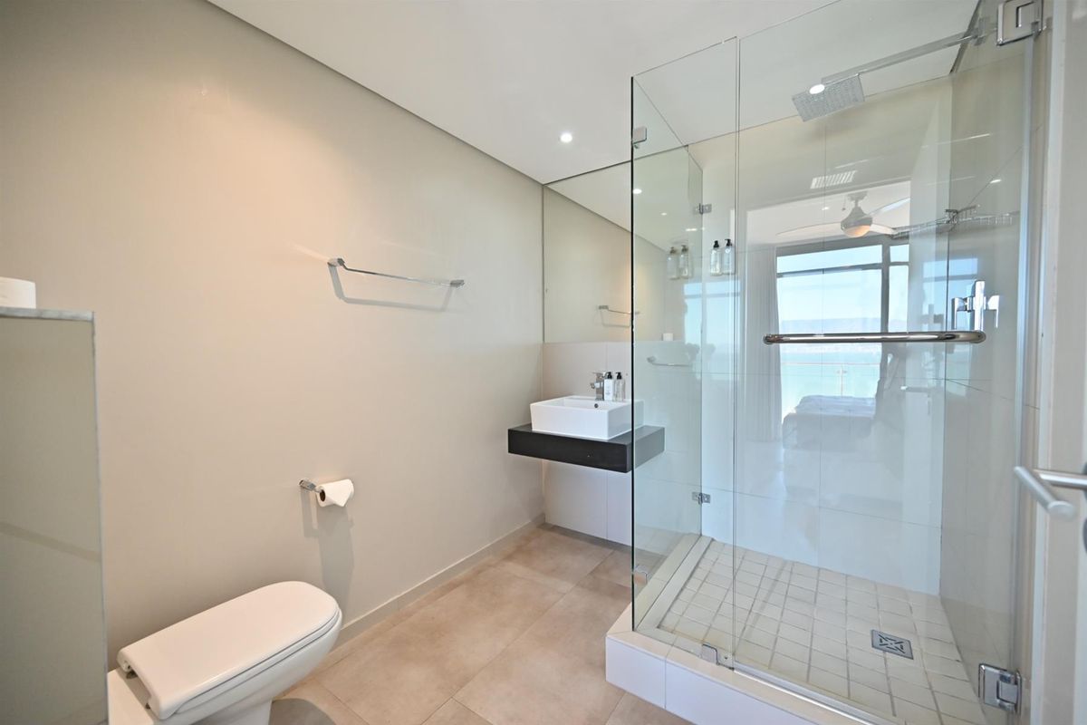 Modern bathroom featuring a glass-enclosed walk-in shower, wall-mounted vanity with vessel sink, and neutral floor tiling.
