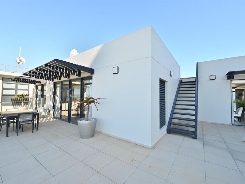 Spacious penthouse rooftop terrace featuring tiled flooring, a modern pergola, external staircase, and glass balustrades with panoramic views.