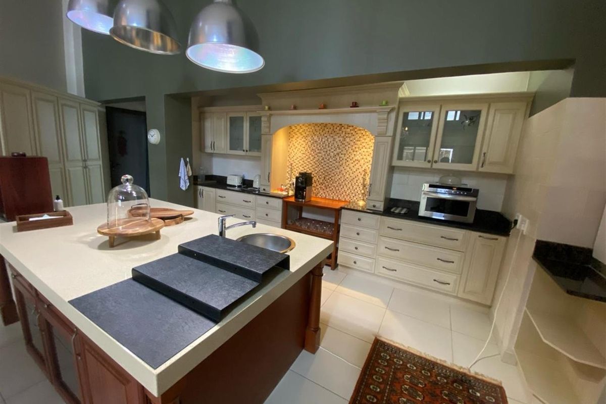 Spacious kitchen featuring a large central island with a prep sink, custom cabinetry, granite countertops, and a decorative tiled backsplash.
