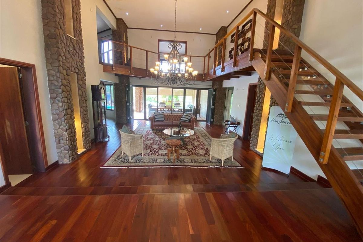 Spacious double-volume living area featuring rich hardwood flooring, stone-clad feature pillars, a grand staircase, and a mezzanine gallery overlooking the main space.