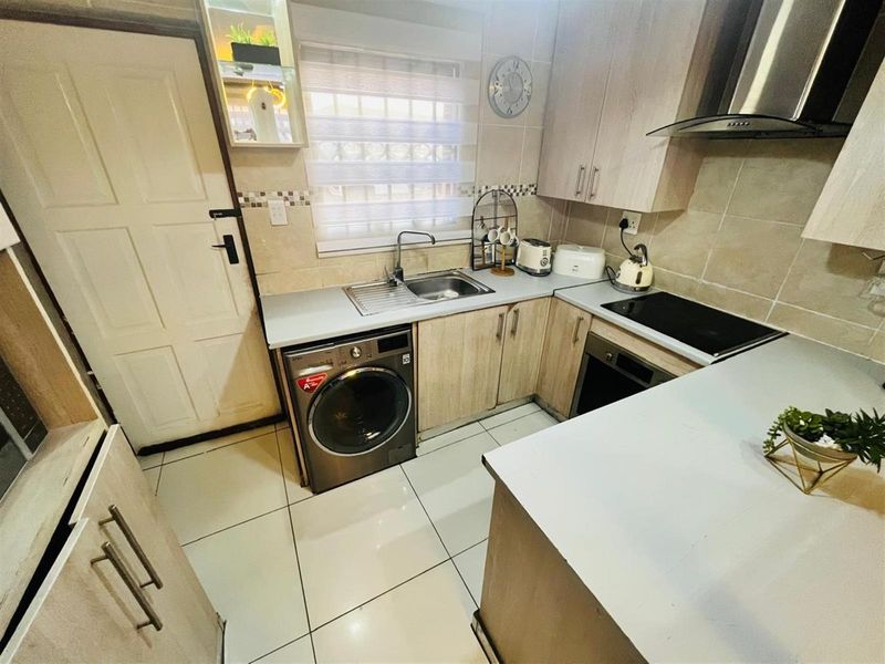 Compact kitchen featuring light wood cabinetry, tiled flooring, a built-in oven with hob, extractor fan, and integrated laundry appliance space.