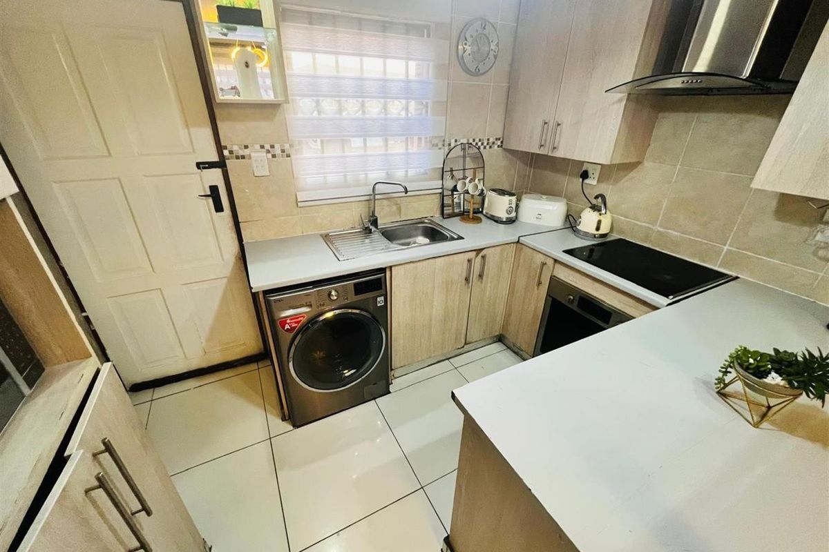 Compact kitchen featuring light wood cabinetry, tiled flooring, a built-in oven with hob, extractor fan, and integrated laundry appliance space.