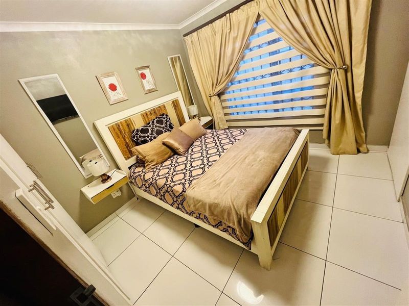 A well-maintained bedroom featuring tiled flooring, neutral wall finishes, and built-in window treatments.