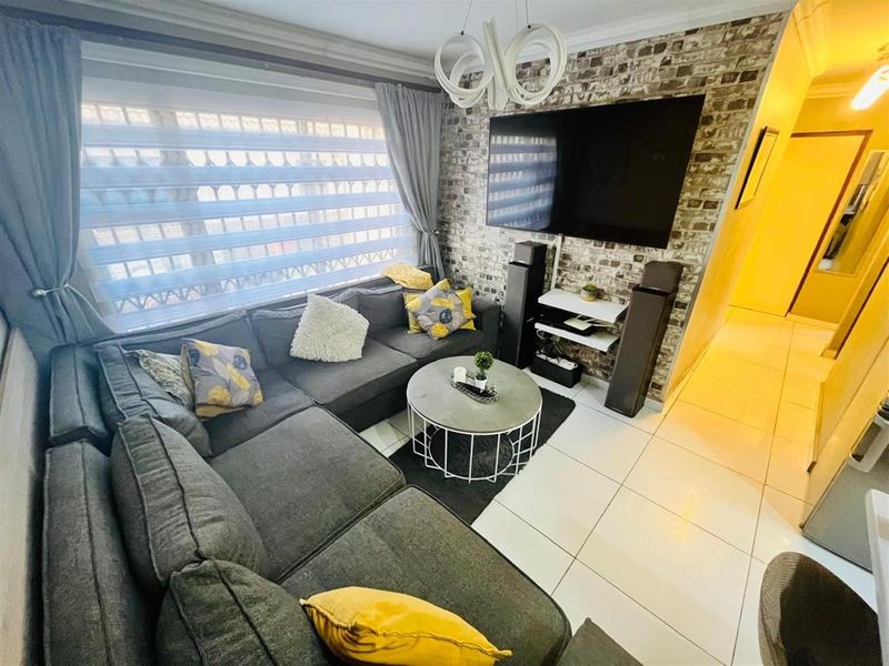 A cozy living room featuring a brick-style feature wall, large window with blinds, and polished floor tiles.