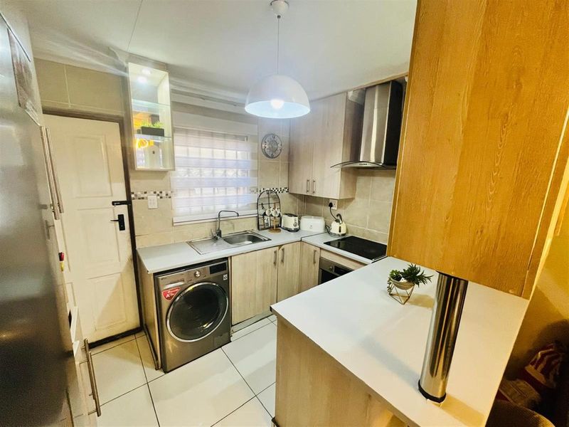 Compact kitchen featuring light wood cabinetry, tiled flooring, built-in oven, hob, extractor fan, and integrated laundry appliance space.