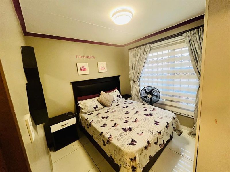 A compact bedroom featuring tiled flooring, a window with fitted blinds, and a ceiling-mounted light fixture.