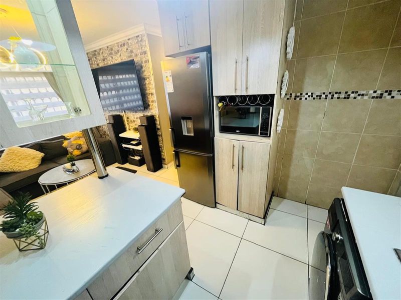 Compact open-plan kitchen featuring light wood cabinetry, tiled flooring, and integrated storage, seamlessly flowing into the adjacent living area.
