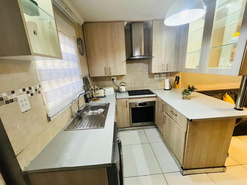 A compact, functional kitchen featuring light wood-finish cabinetry, a built-in oven, extractor fan, and tiled flooring with a breakfast counter.
