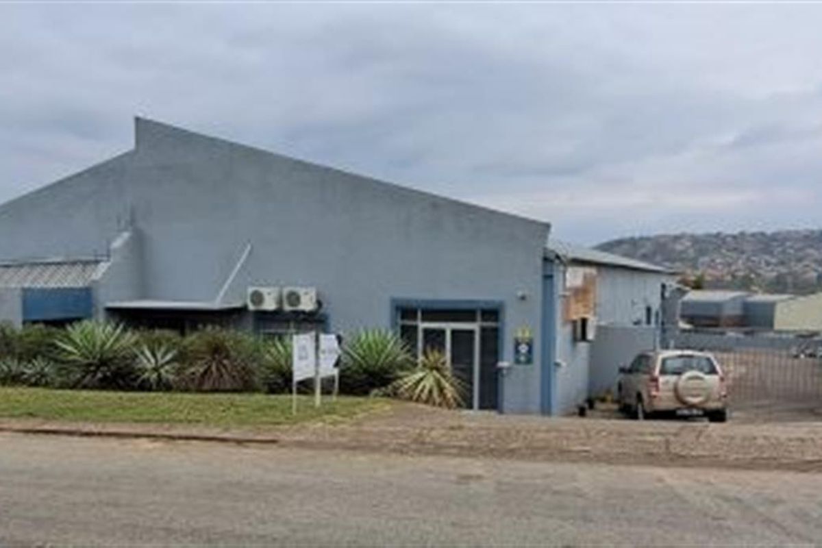 Exterior view of a commercial warehouse building featuring a pitched roof, perimeter wall, and gated access point.