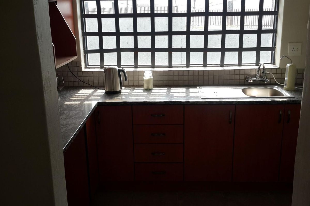 A functional kitchen area featuring dark wood cabinetry, a stone-look countertop, a stainless steel sink, and a window with security bars.