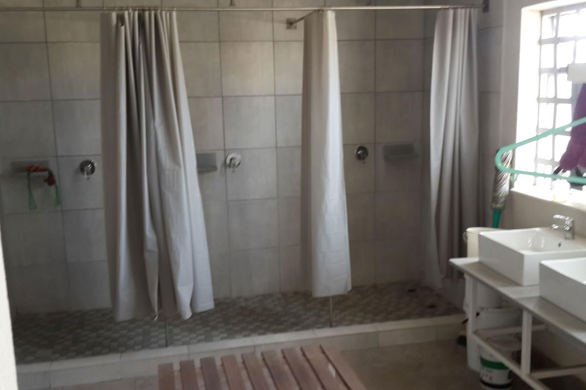 Communal bathroom area featuring multiple shower stalls with tiled walls and dual vessel sinks on a vanity unit.