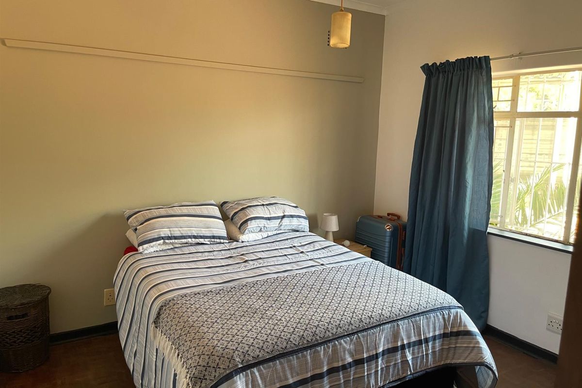 A functional bedroom featuring parquet flooring, a window with curtain track, and neutral wall finishes.