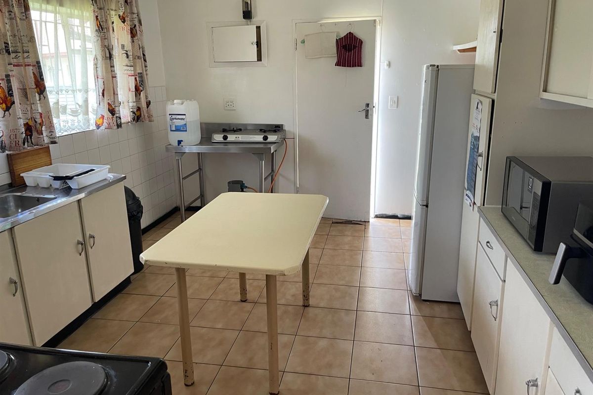 A functional kitchen featuring tiled flooring, basic cabinetry, and a stainless steel prep station with a gas hob.