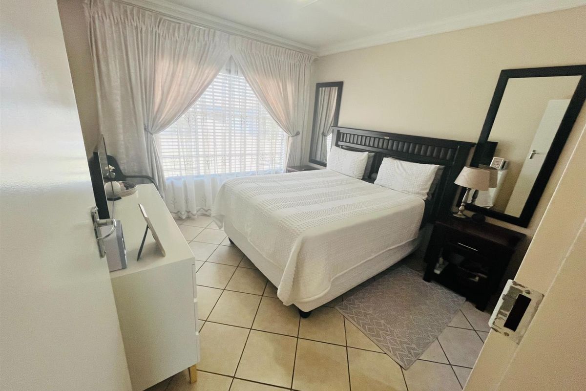 A well-lit bedroom featuring tiled flooring, neutral wall finishes, and large windows with curtain treatments.