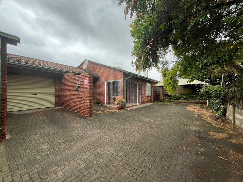 Front exterior view of a brick townhouse featuring a single garage, paved driveway, and security bars on windows.