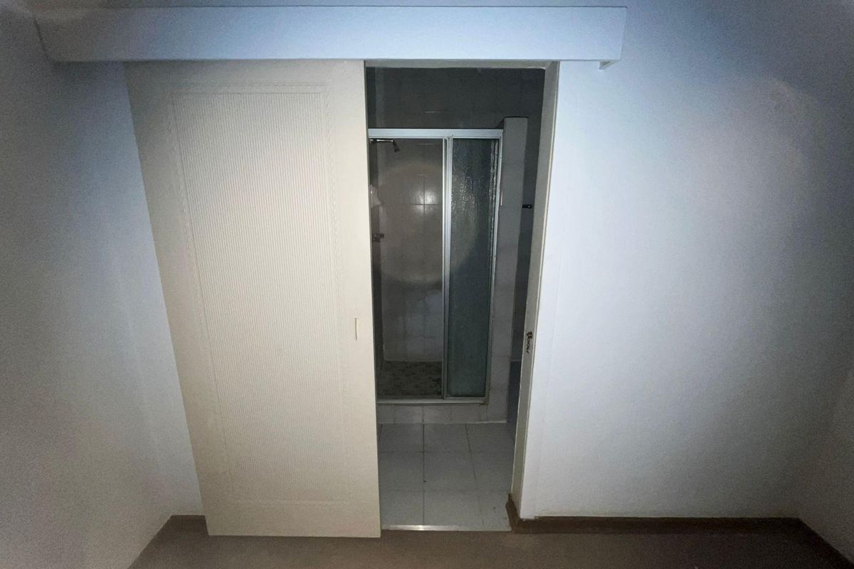 A view into a small en-suite bathroom featuring a shower enclosure, accessed via a sliding door from the adjacent room.