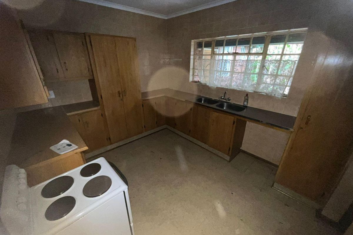 A dated kitchen featuring original wooden cabinetry, a double basin sink, and a freestanding electric stove, offering potential for a modern renovation.