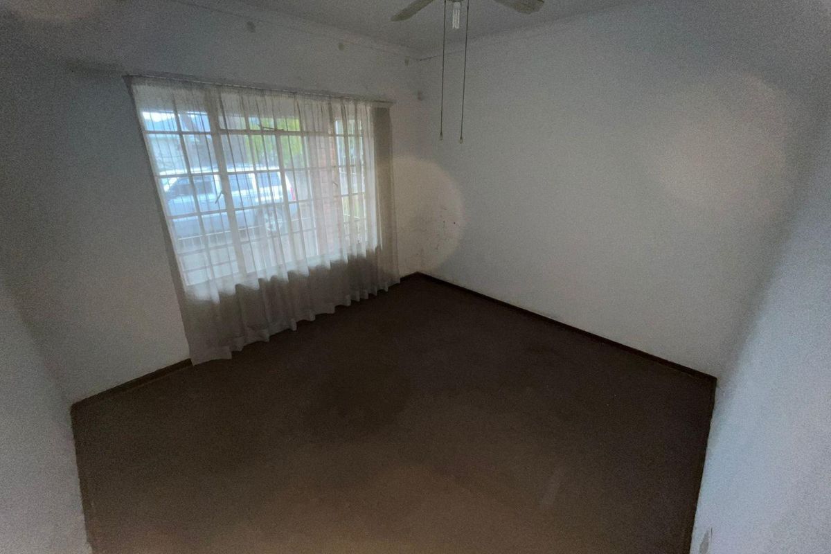 An empty bedroom featuring a ceiling fan, large window with curtains, and carpeted flooring, offering a blank canvas for renovation.