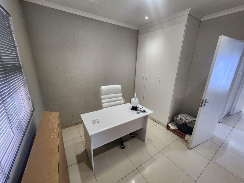 A functional office space featuring tiled flooring, built-in wardrobe storage, and venetian blinds, providing a clean and neutral workspace.