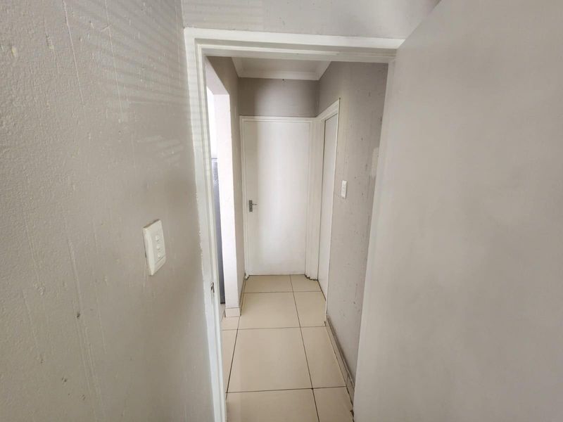 A simple, empty hallway featuring tiled flooring and neutral wall finishes, providing access to adjacent rooms within the apartment.