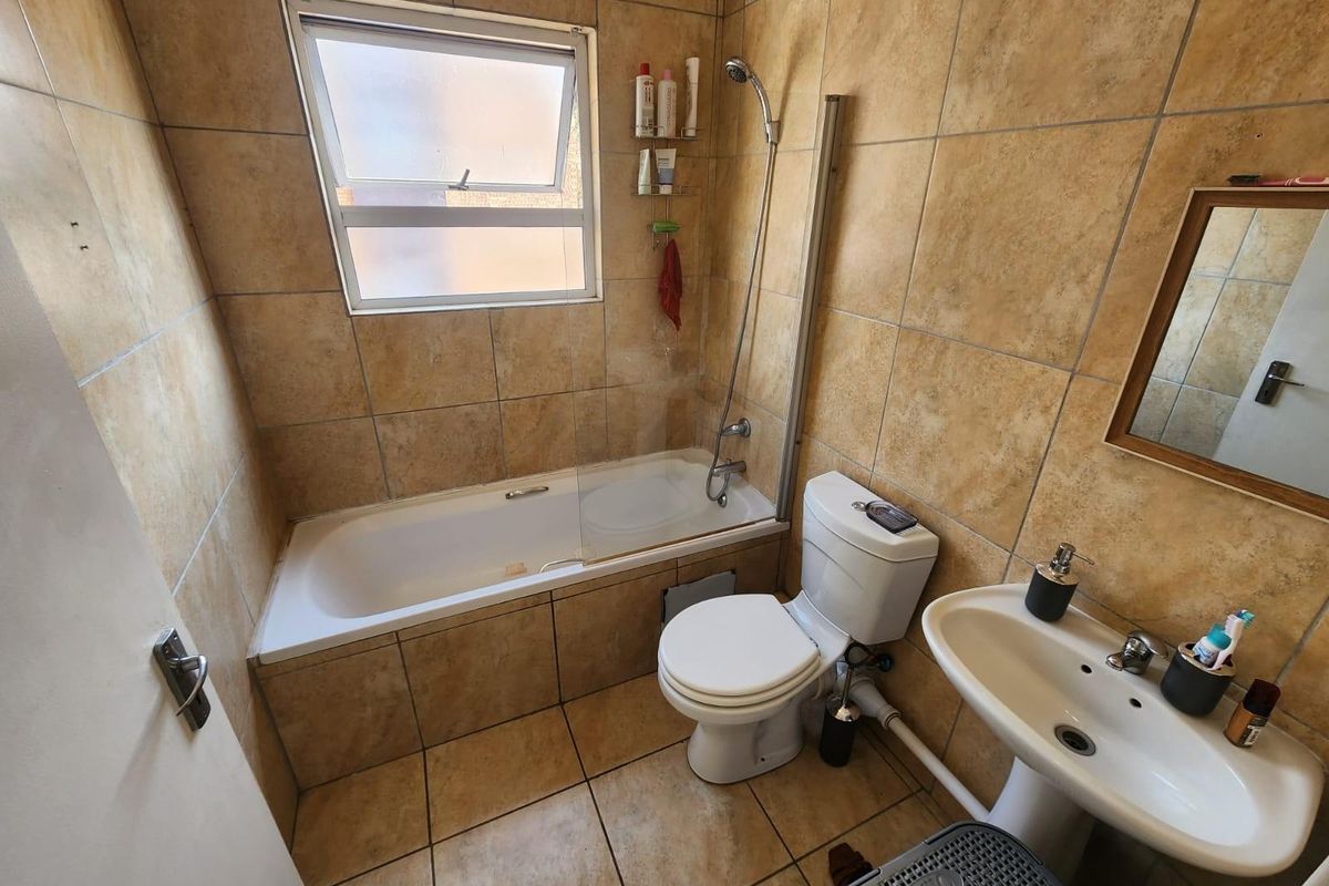 A functional bathroom featuring a bathtub with a shower mixer, glass screen, pedestal basin, and toilet, finished with neutral floor-to-ceiling wall tiles.