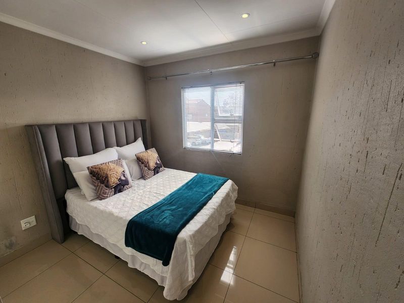 A well-maintained bedroom featuring neutral textured walls, tiled flooring, recessed lighting, and a window fitted with venetian blinds.
