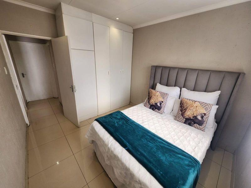 A well-maintained bedroom featuring neutral tiled flooring, built-in white cupboards, and a modern grey upholstered headboard.